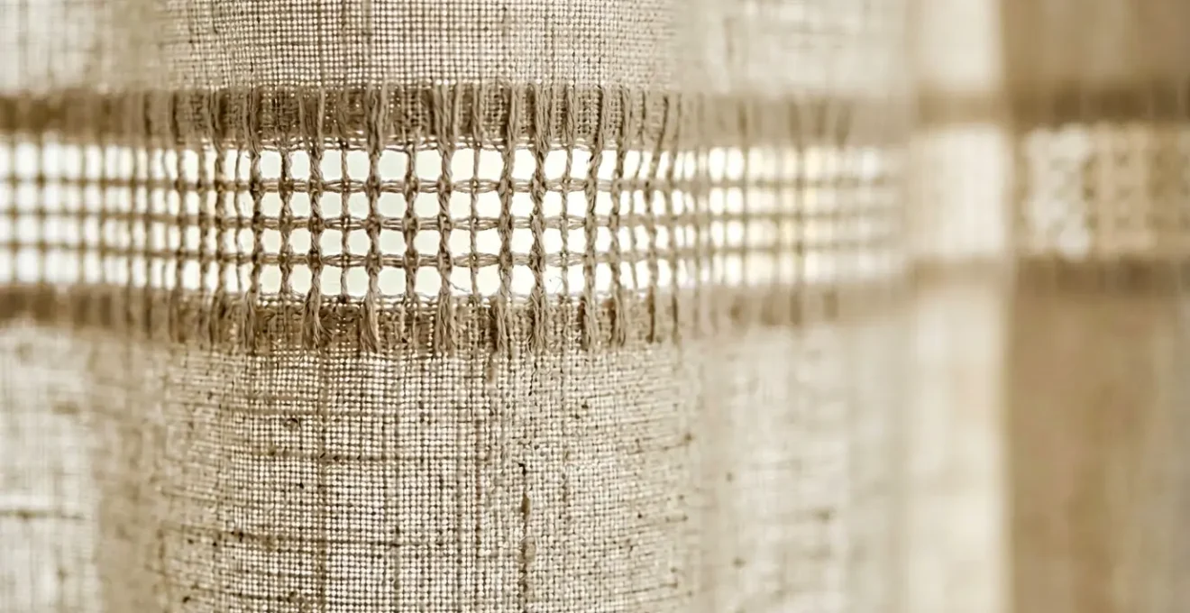 Dettaglio di orlo a giorno su tenda in lino con luce naturale che filtra attraverso la trama