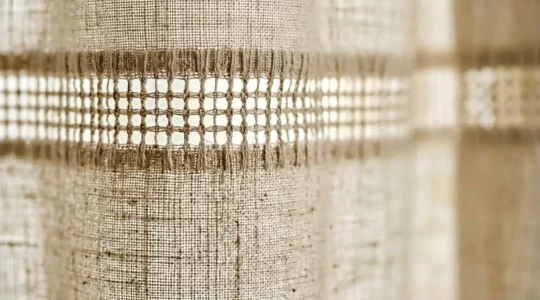 Dettaglio di orlo a giorno su tenda in lino con luce naturale che filtra attraverso la trama